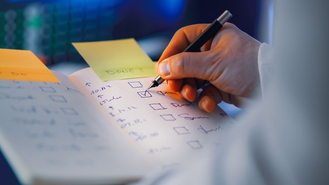 Hand checking off completed items on a handwritten checklist with sticky notes