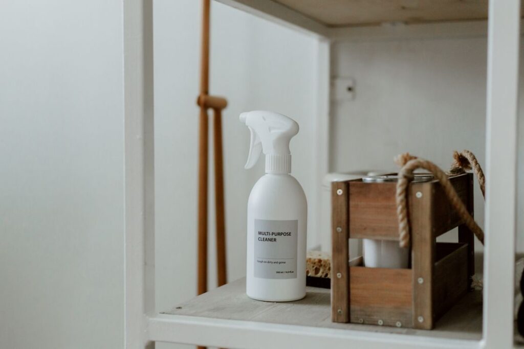 A reusable multi-purpose cleaner spray bottle and natural cleaning supplies arranged on a wooden shelf