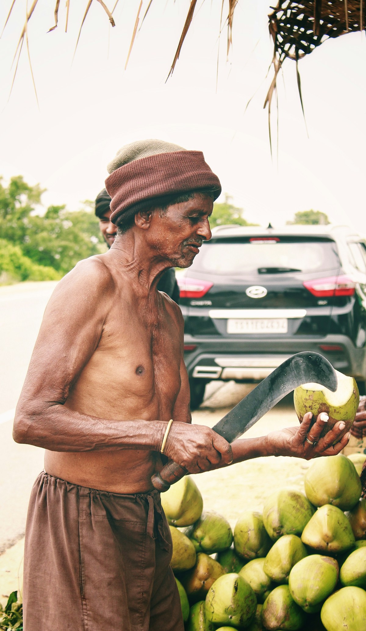 An Indian vendor opening fresh green tender coconuts