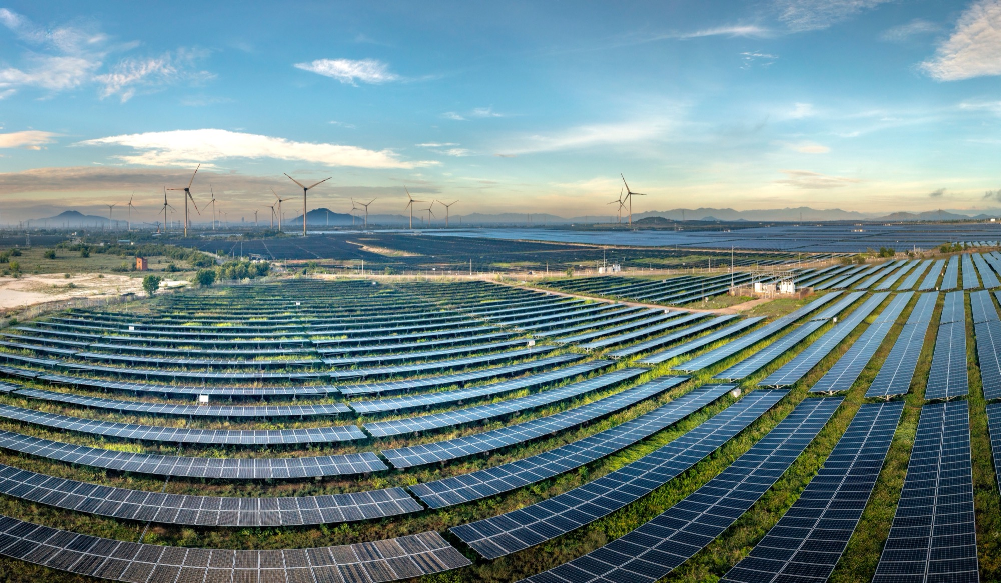 Wide landscape view of a solar farm with wind turbines in the background, representing India renewable energy capacity growth