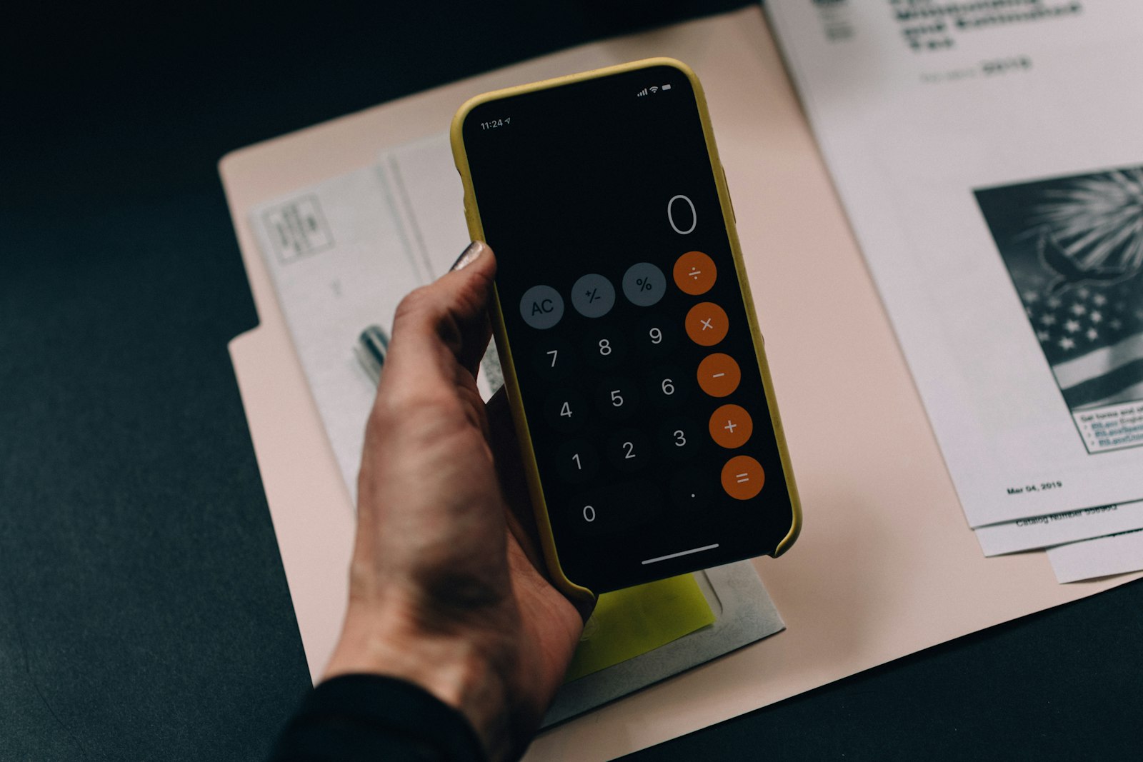 Hand holding a calculator over paper utility bills and folders, representing manual carbon accounting record-keeping