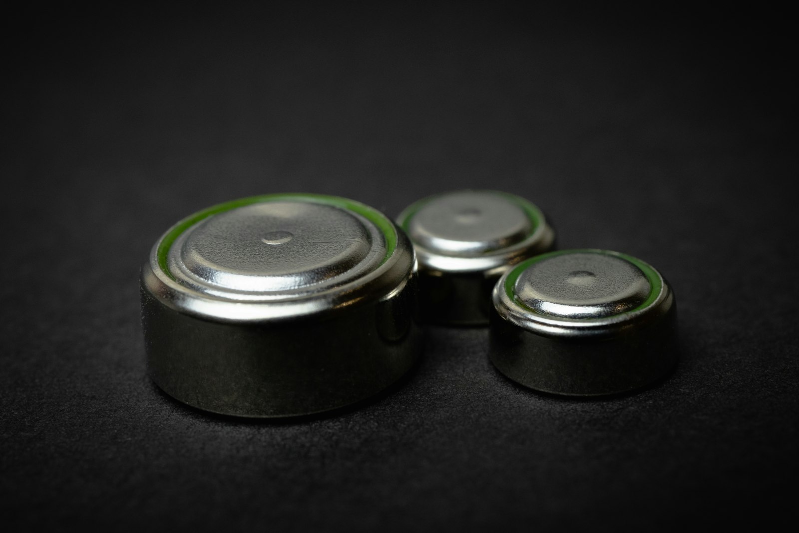 Close-up of three coin-cell batteries on a black background, representative of the coin-cell battery format used to test the new cobalt-free organic battery material