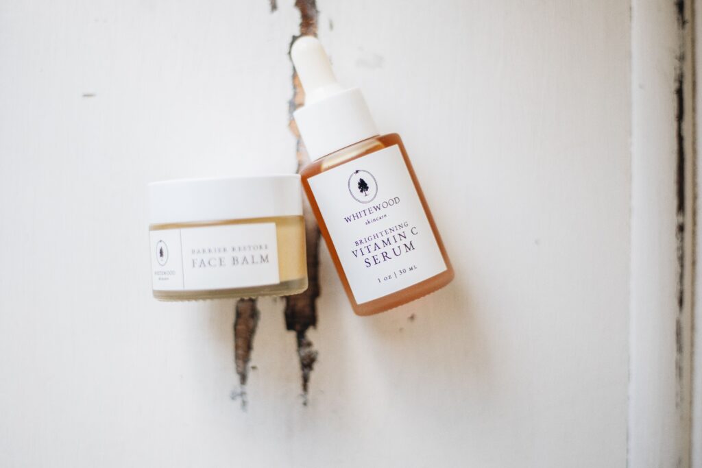 Natural organic skincare face balm and vitamin C serum bottles on a rustic white wooden background