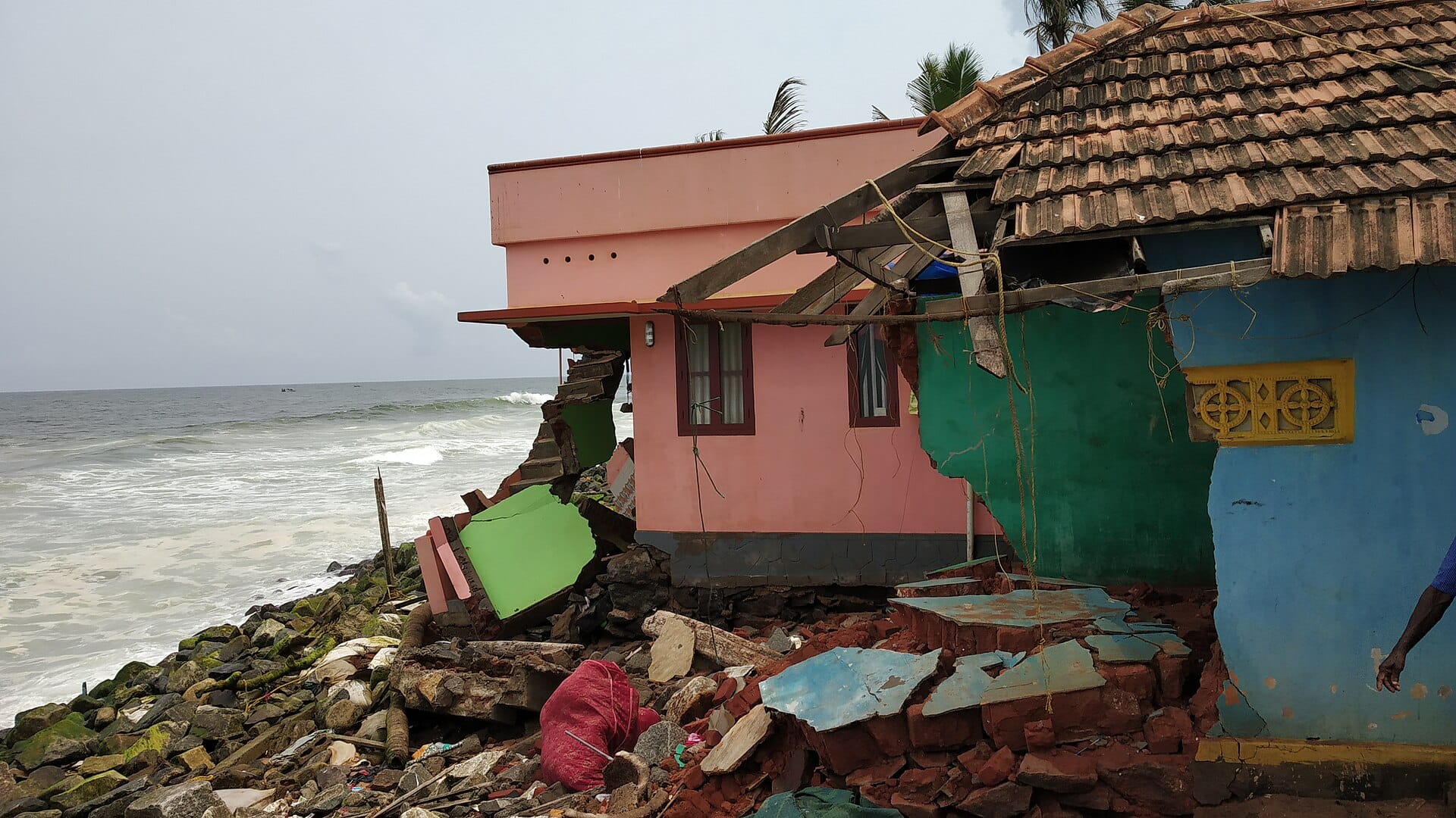 Waves and a rock seawall beside a house damaged by coastal erosion at Valiyathura, Kerala