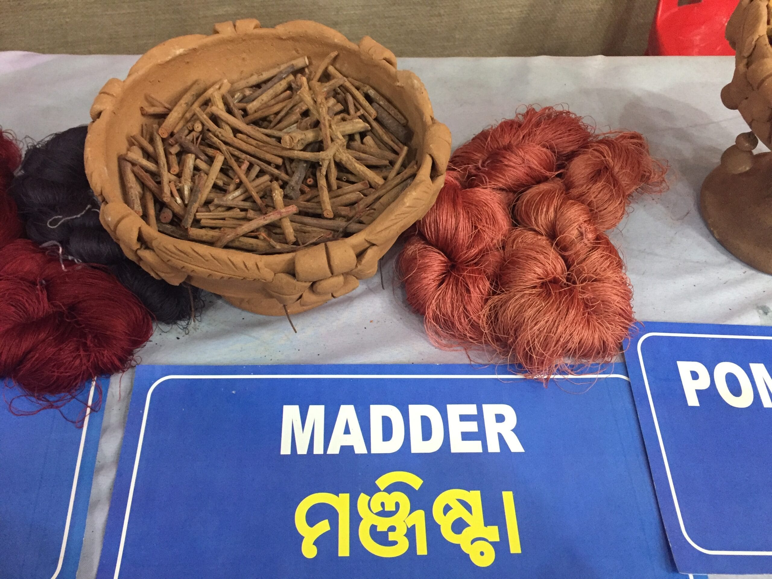 Dried madder (manjistha) roots in a clay bowl beside silk yarn dyed a natural red