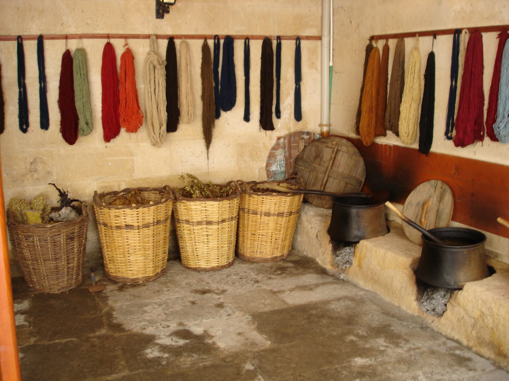 Skeins of yarn dyed with natural plant dyes hanging beside baskets of dye plants and dye pots